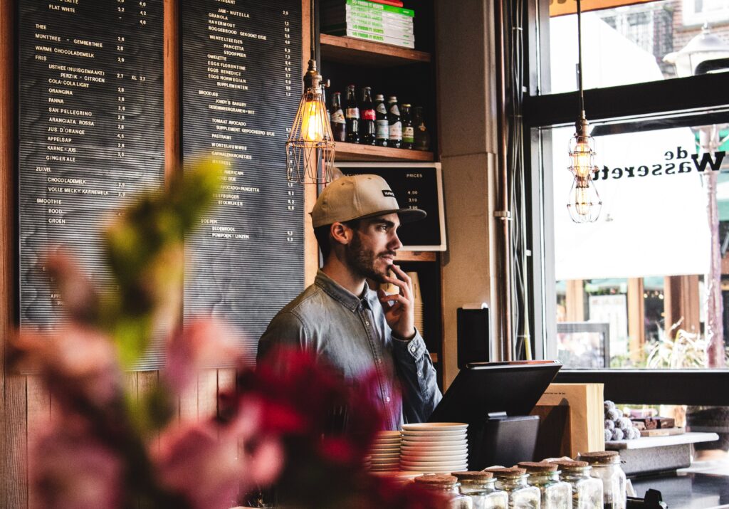 man wearing brown cap in across menu board - Photo by Louis Hansel on Unsplash