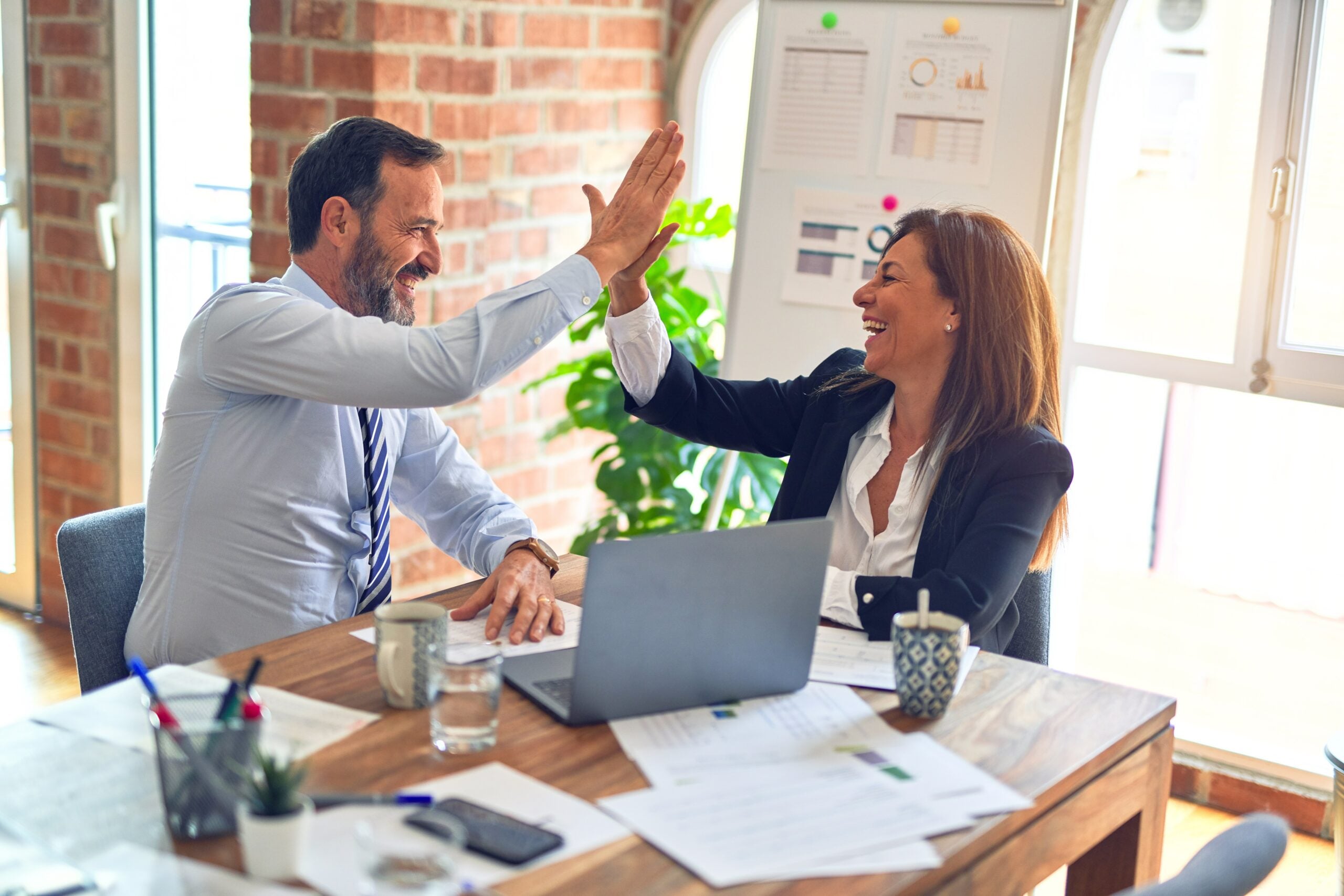 People Developent: Two middle age business workers smiling happy and confident. Working together with smile on face hand giving high five at the office